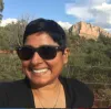 Woman smiling in front of a small mountain and large bushes